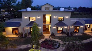 A two-story house with a central staircase, multiple windows with exterior lighting, and a well-maintained garden. - Clarissa Resort (Ramnagar)