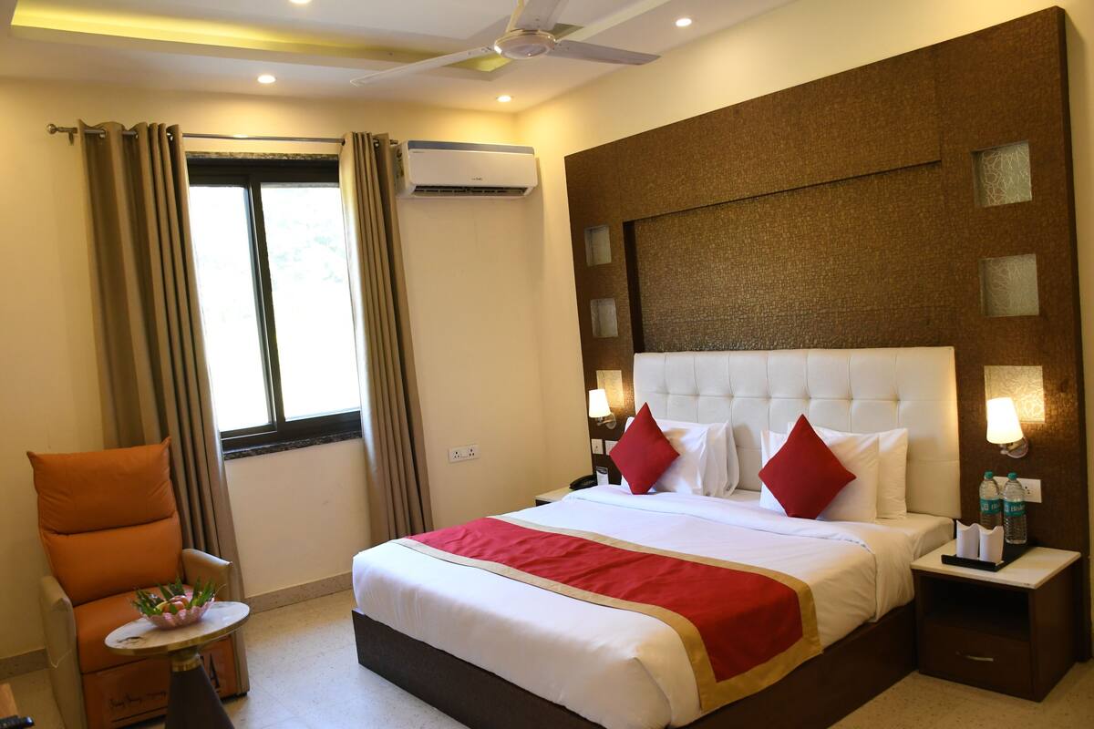 Quarto de hotel com uma cama grande, uma cadeira, uma mesa pequena e um ar condicionado.