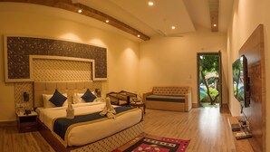 A spacious bedroom with a large bed, a sitting area, and a television. - Clarissa Resort (Ramnagar)