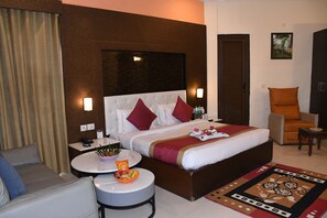 A hotel room with a large bed, a sofa, a round table, and a chair. - Clarissa Resort (Ramnagar)
