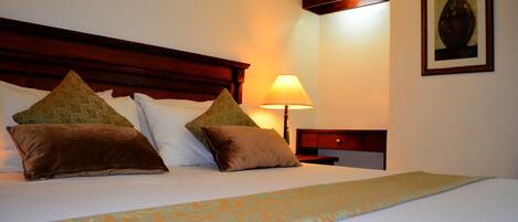 A neatly made bed with patterned bedding, a bedside lamp, and a framed artwork on the wall.