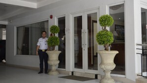 A hotel entrance with a receptionist, a glass door, and two large planters with topiary trees. - Grand Isabella Residences (Cebu City)
