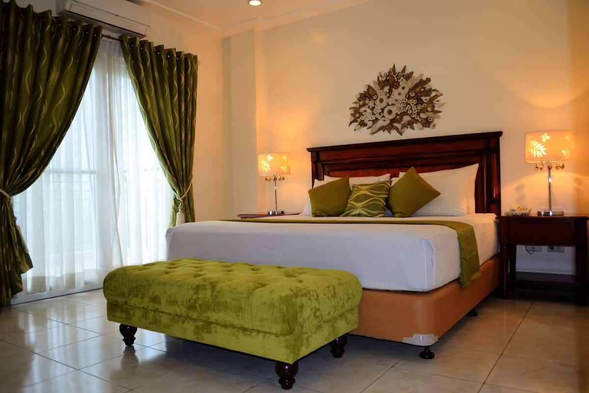 Habitación de hotel con una cama grande, un reposapiés verde, dos lámparas de noche y un adorno en la pared.