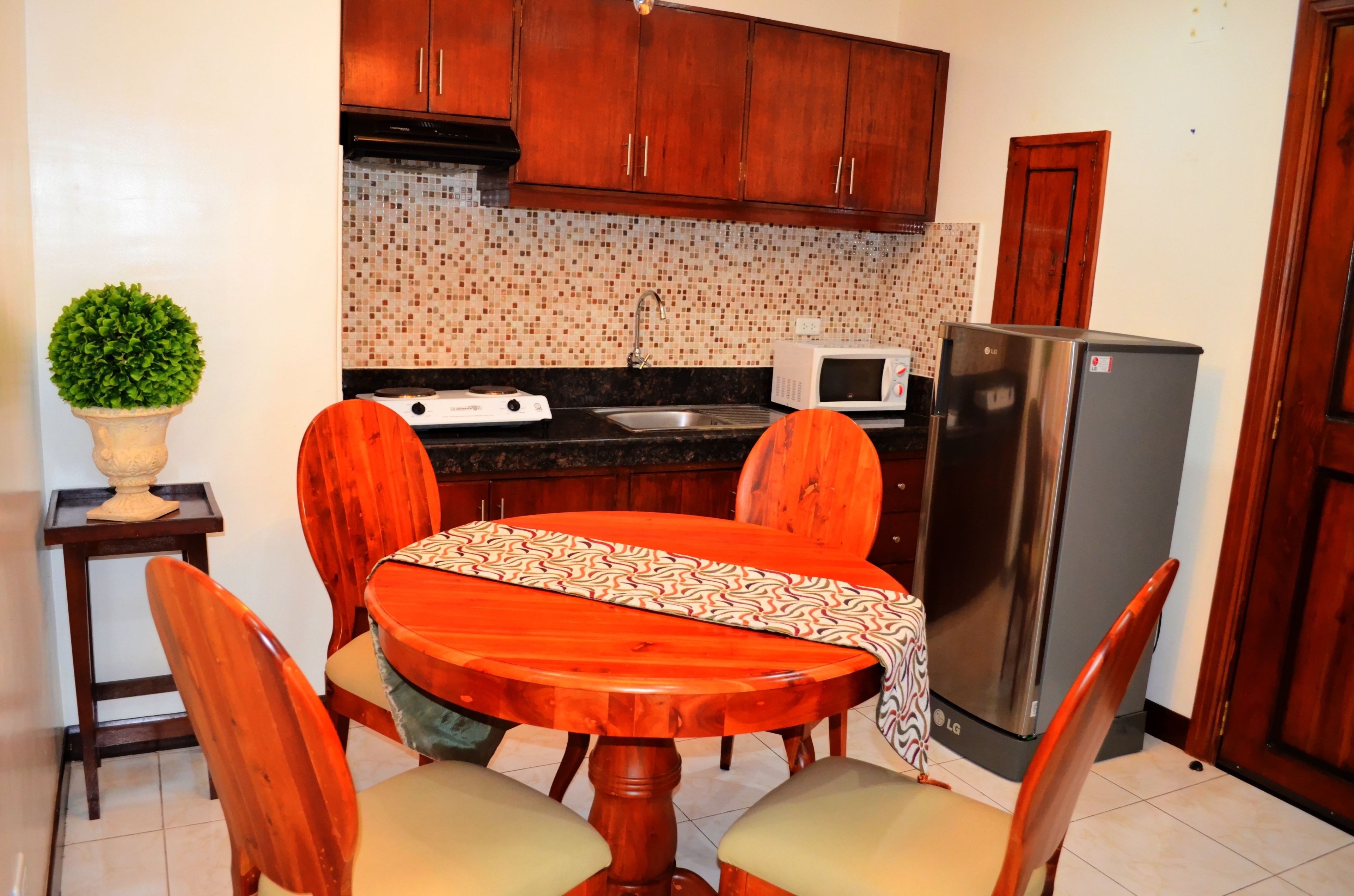 A compact kitchen with wooden cabinets, a microwave, a refrigerator, and a dining table with chairs.