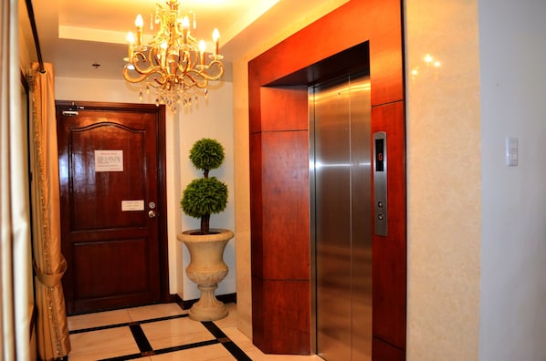 Un hall d’hôtel avec une porte en bois, une plante en pot, un lustre et un ascenseur moderne.