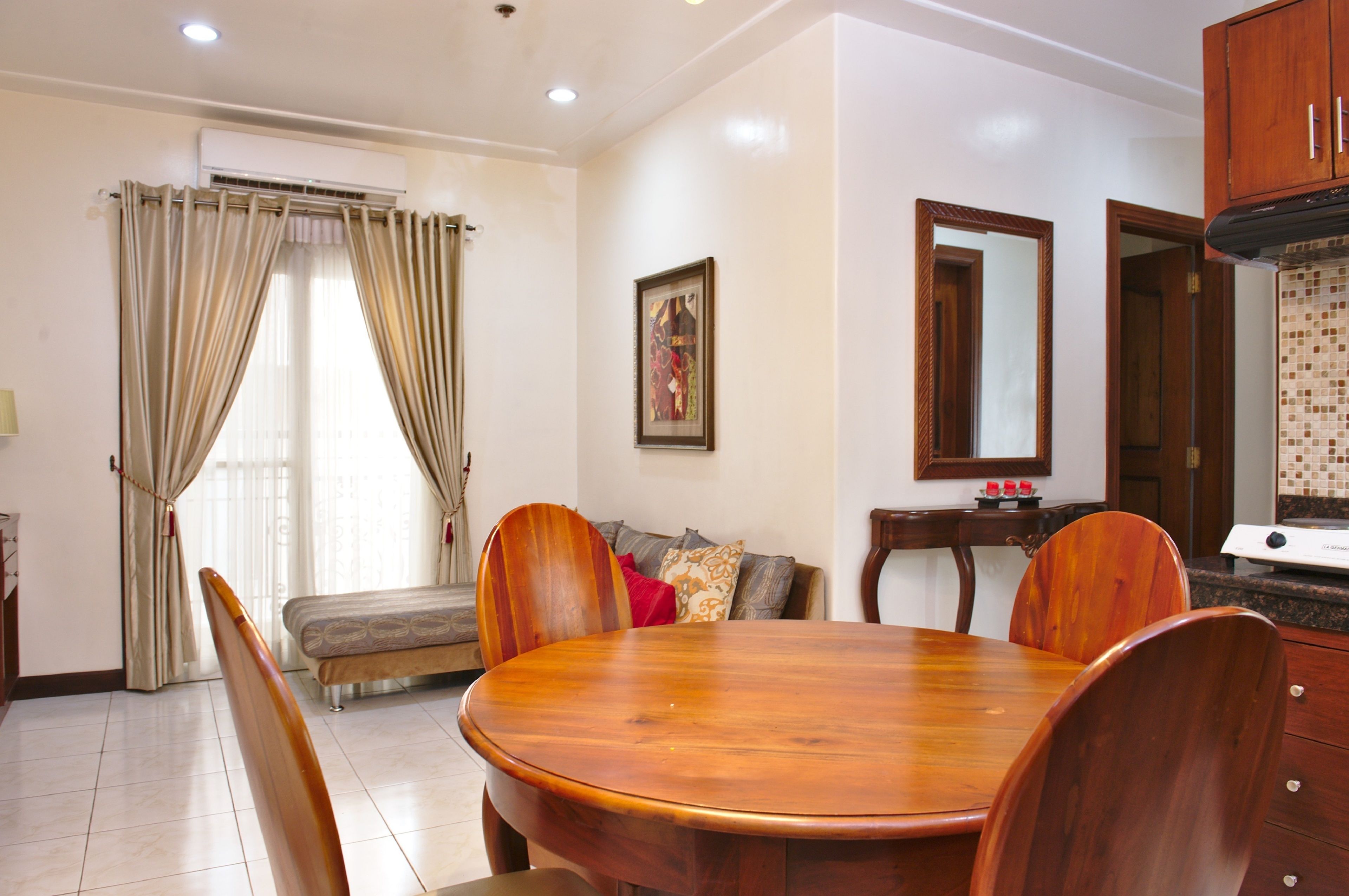Un área de comedor con una mesa redonda de madera, cuatro sillas de madera, un sofá con cojines y una cocina con estufa y armarios.