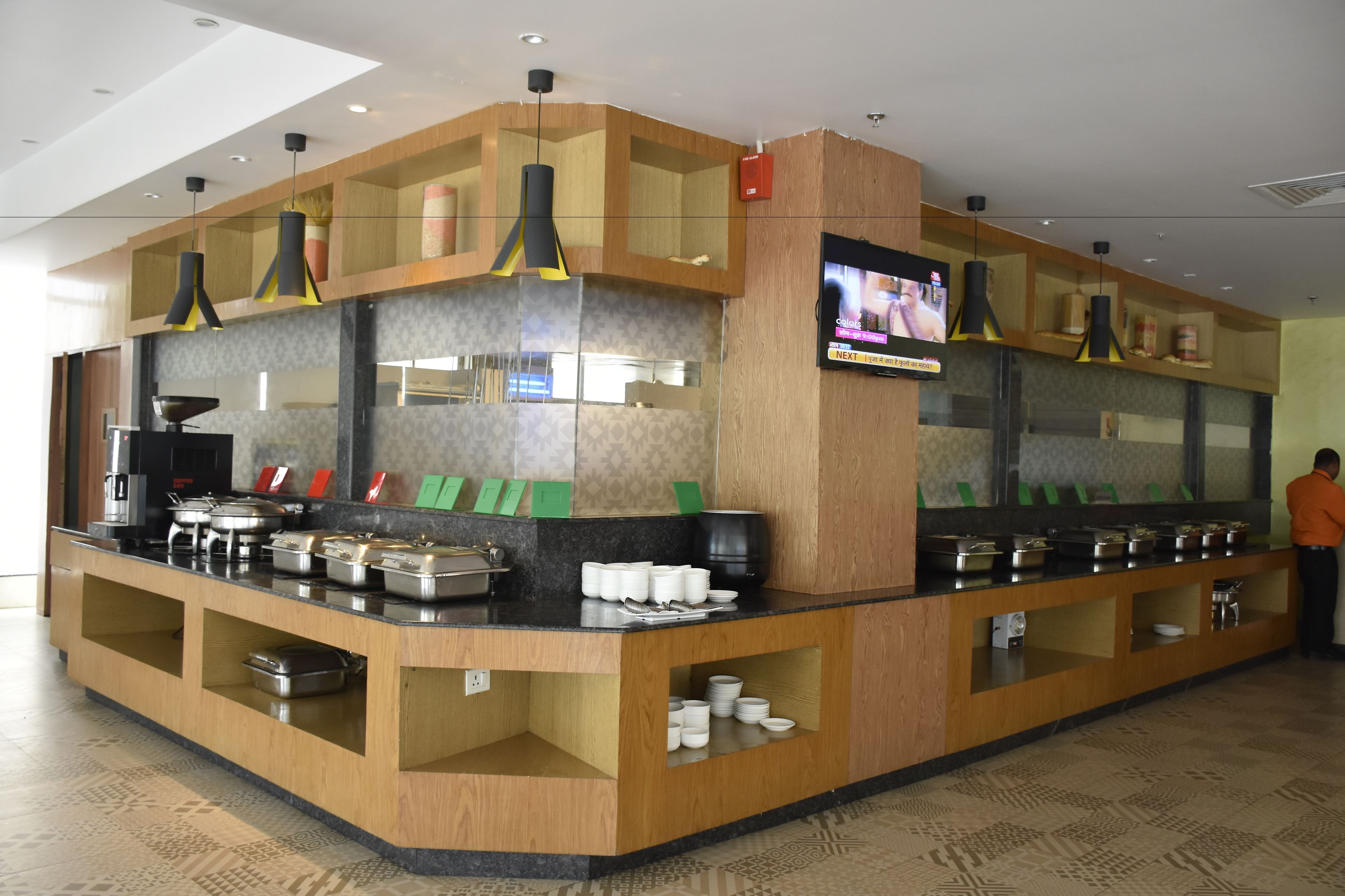 A buffet area with multiple serving stations, a television screen, and a person in an orange shirt.