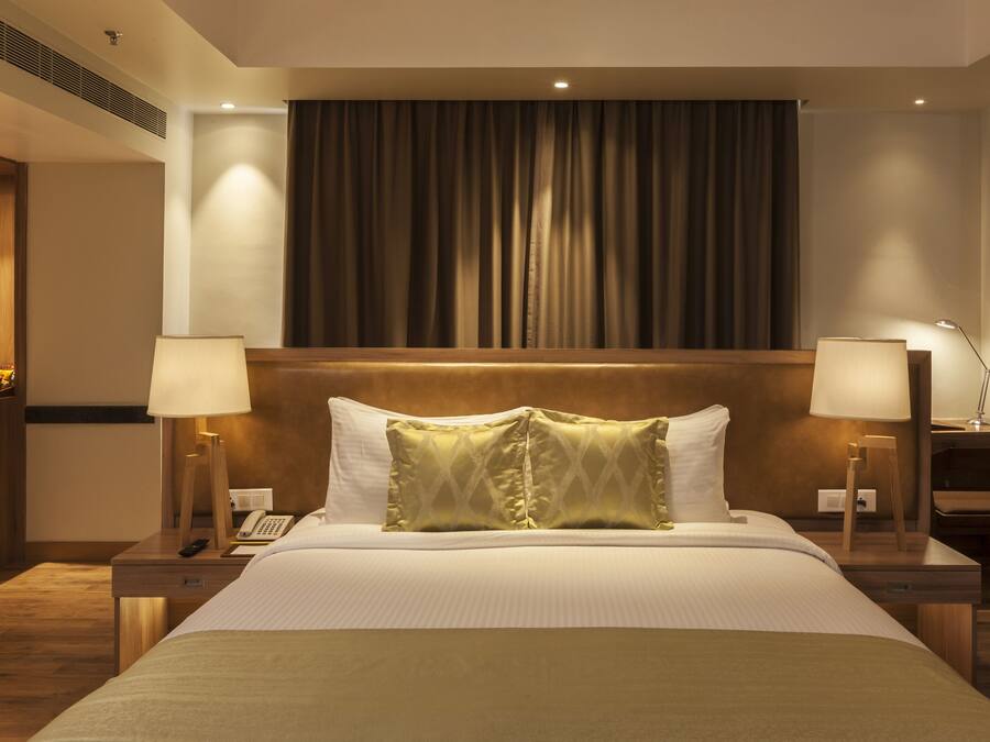 Una habitación de hotel con una cama grande, dos mesitas de noche con lámparas, un armario de madera y una cortina.