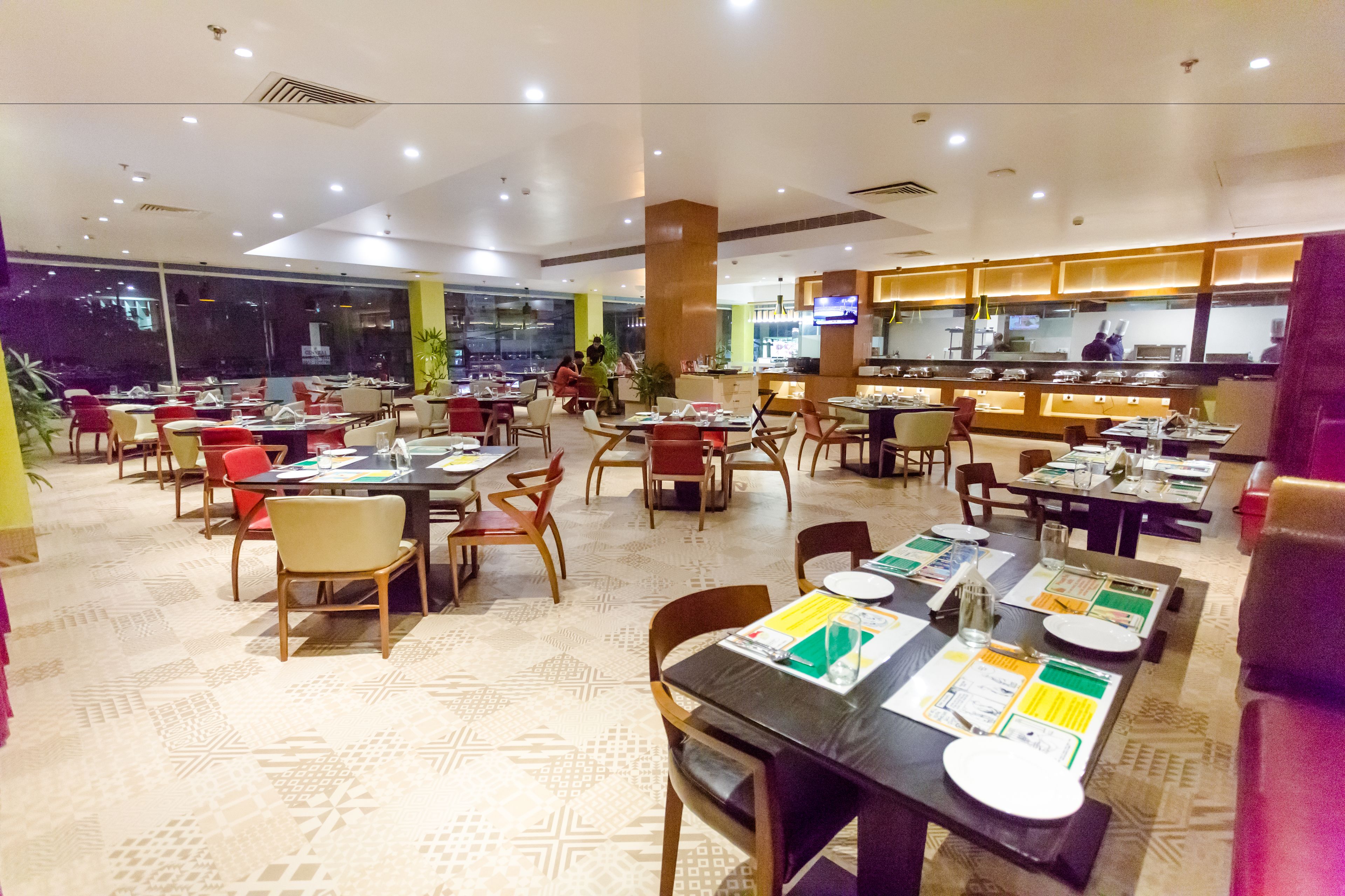 A spacious restaurant with multiple dining tables and chairs, a large window, and a counter with a television.