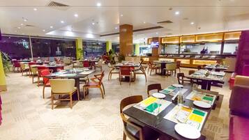 A spacious restaurant with multiple dining tables and chairs, a large window, and a counter with a television.