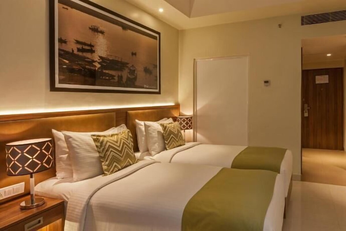 Habitación de hotel con dos camas, una mesita de noche, un armario de madera y un cuadro en la pared.