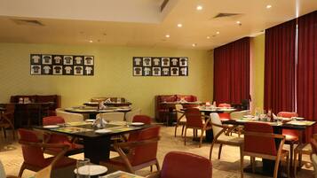 Un restaurant avec de nombreuses tables et chaises, des tableaux encadrés aux murs et des rideaux rouges.
