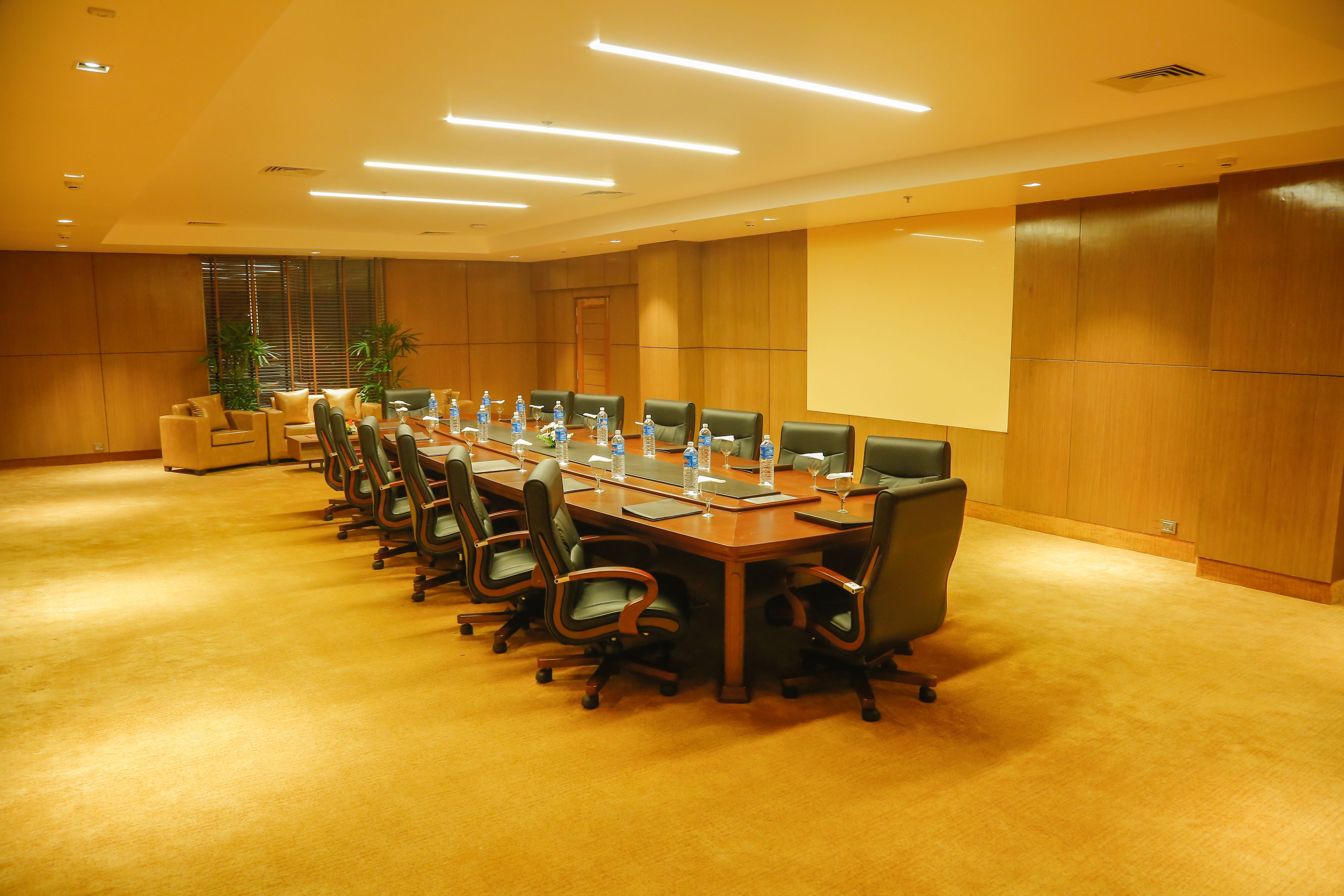 A conference room with a long table, multiple chairs, water bottles, and a projector screen.