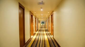 A hotel hallway with a striped carpet, wooden doors, and recessed lighting.