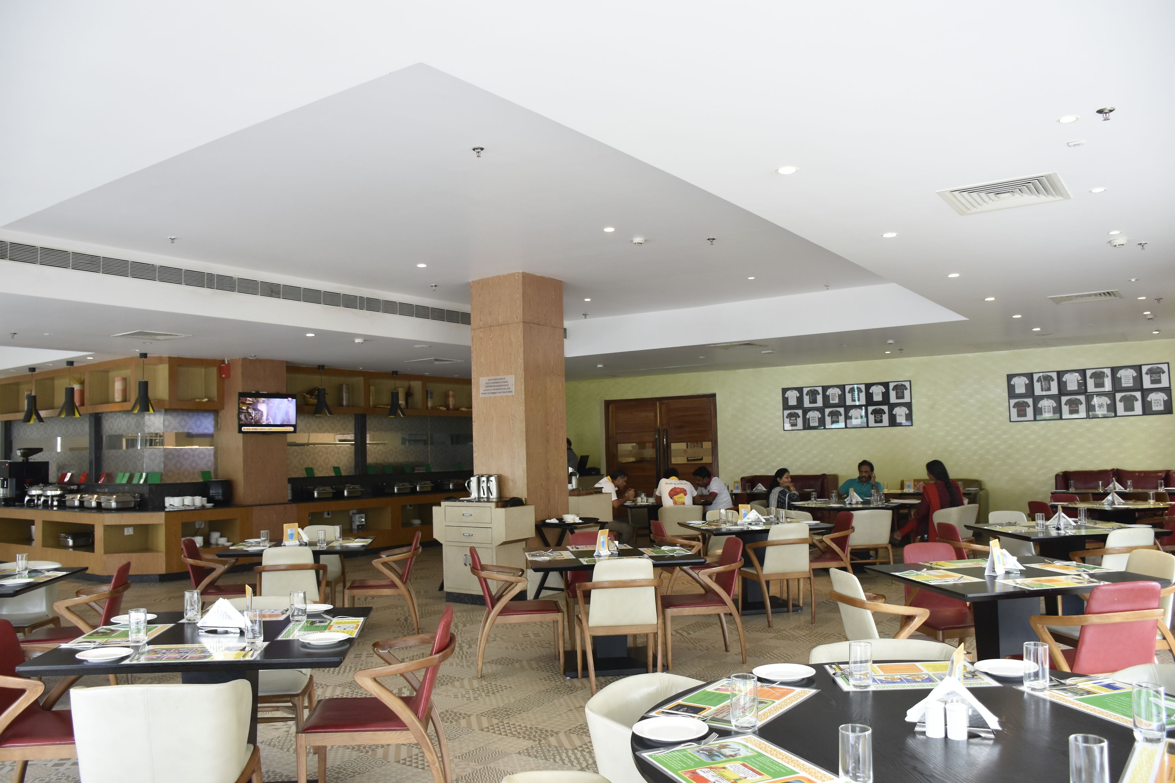 A spacious restaurant with multiple dining tables and chairs, a kitchen area, and a television screen.