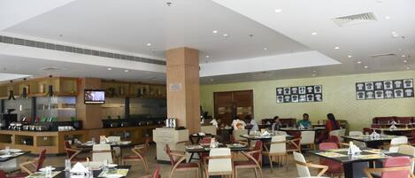 A spacious restaurant with multiple dining tables and chairs, a kitchen area, and a television screen.