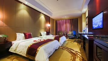 A hotel room with two beds, a desk, a television, and a large window with curtains.