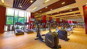 Een sportschool met meerdere loopbanden en elliptische trainers, grote ramen en een houten vloer.