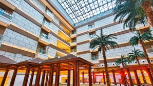 Een meerverdiepings atrium met een glazen dak, palmbomen en houten constructies.
