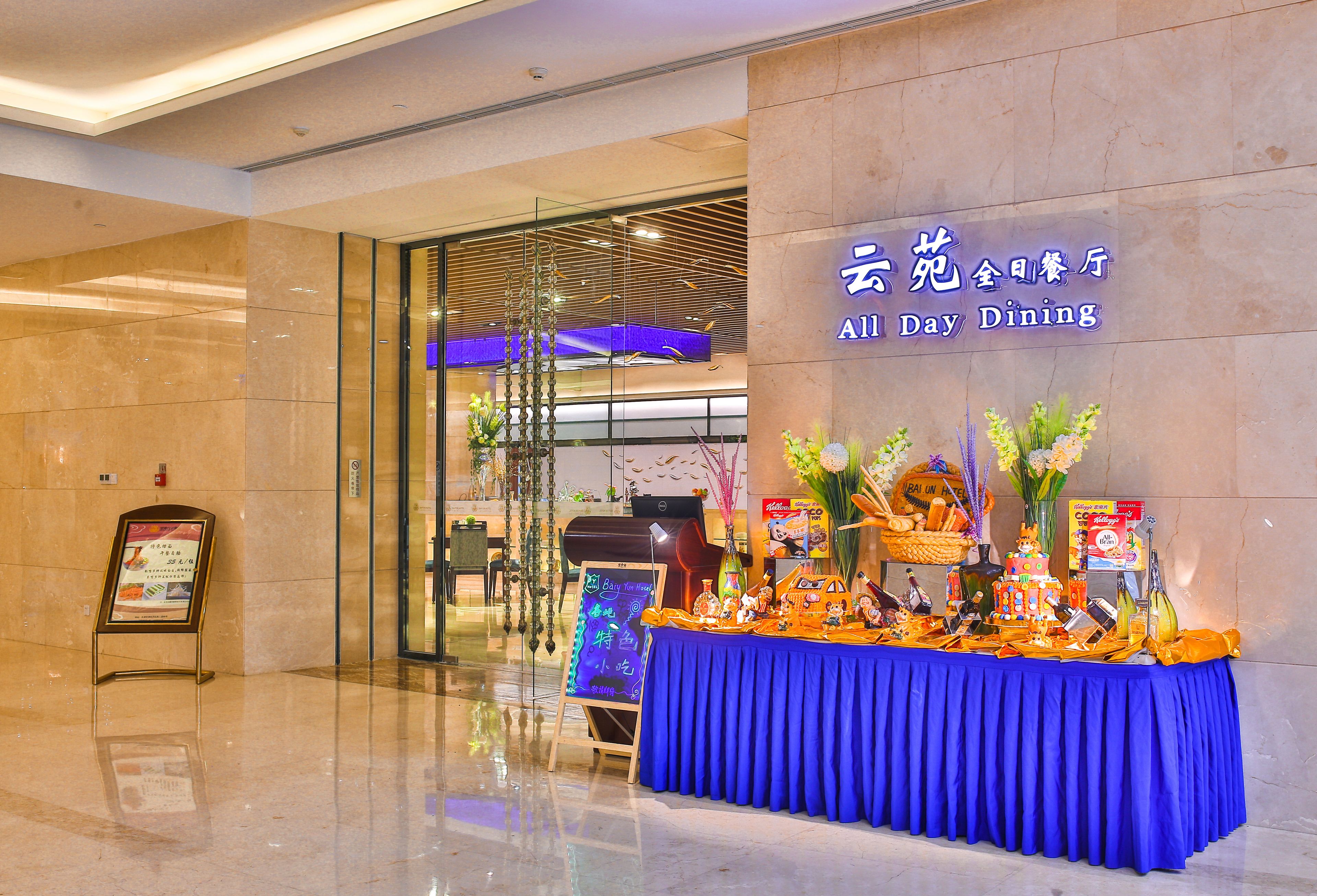 A hotel entrance with a blue table displaying various items and a sign reading "All Day Dining".