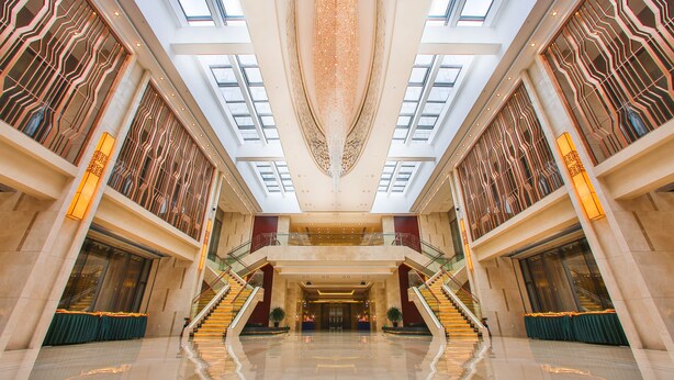 Een ruime lobby met een hoge plafond, grote ramen en een centrale trap.