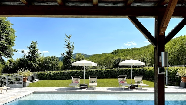 A pool area with lounge chairs and umbrellas, surrounded by a wooden pergola and a view of a green landscape. - Welcome to Lucca and beautiful Villa Adriano! (Valdottavo)