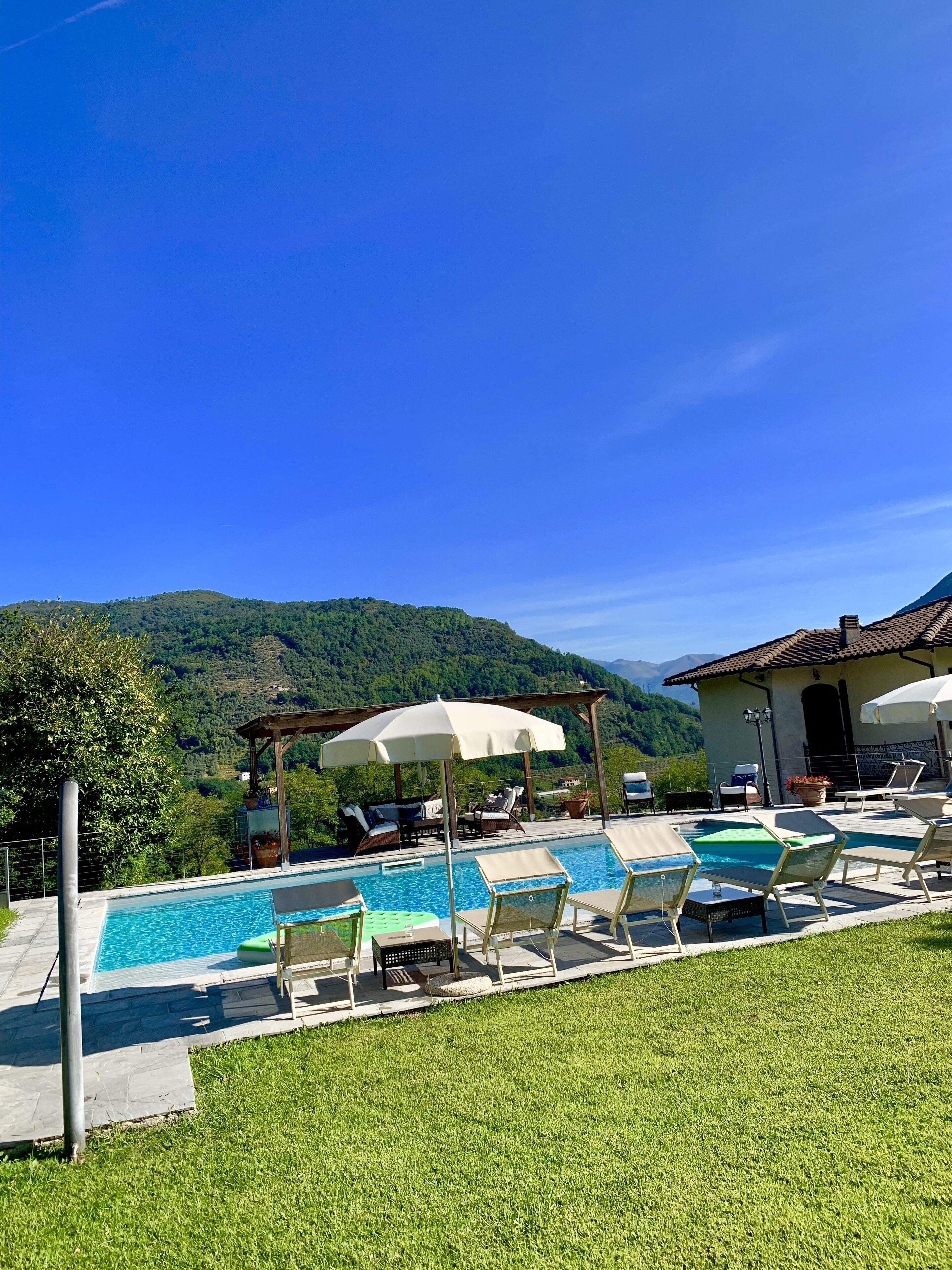 Un espace piscine agrémenté de chaises longues et de parasols, entouré d’une pelouse verdoyante et offrant une vue sur une chaîne de montagnes.
