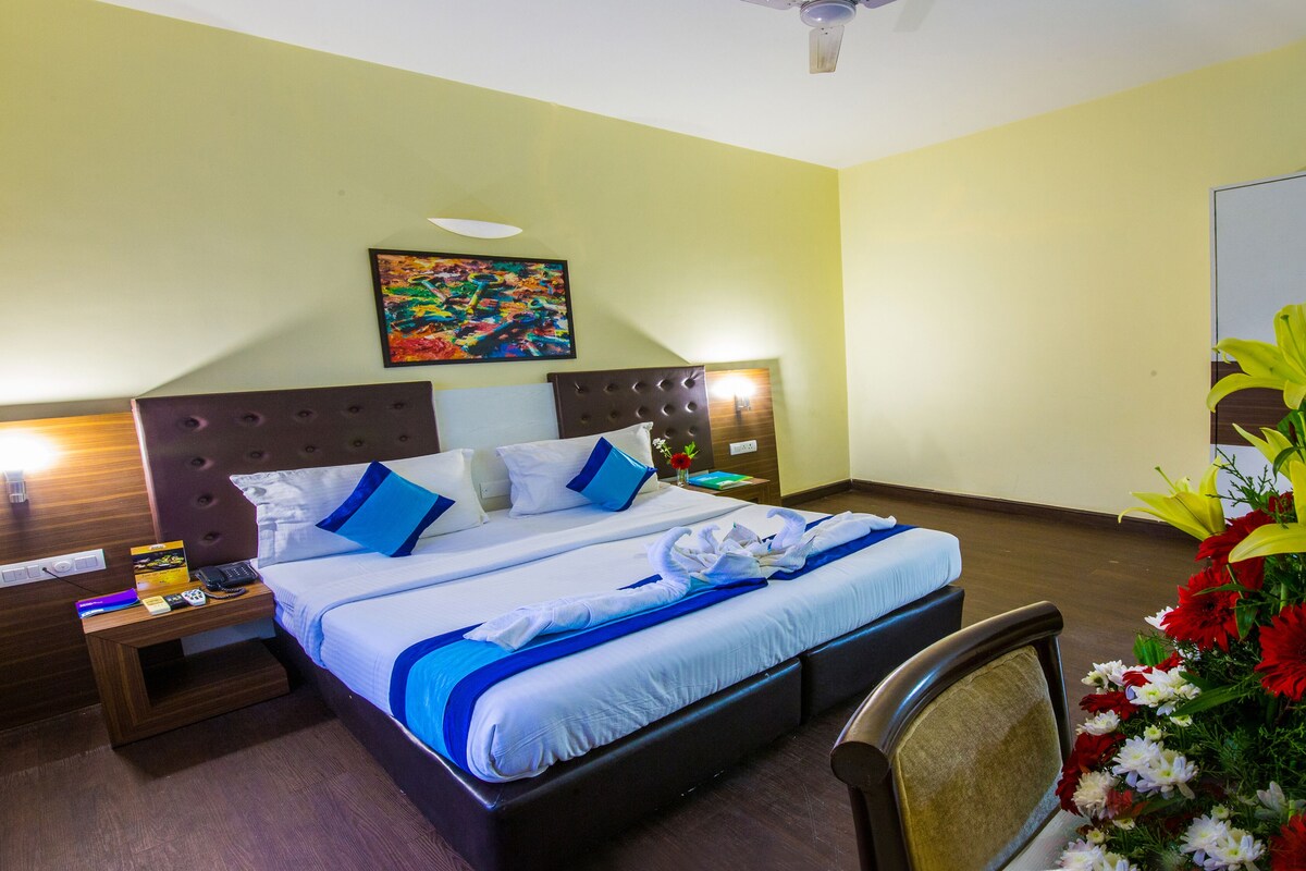 A hotel room with a bed, nightstands, a painting, and a floral arrangement.
