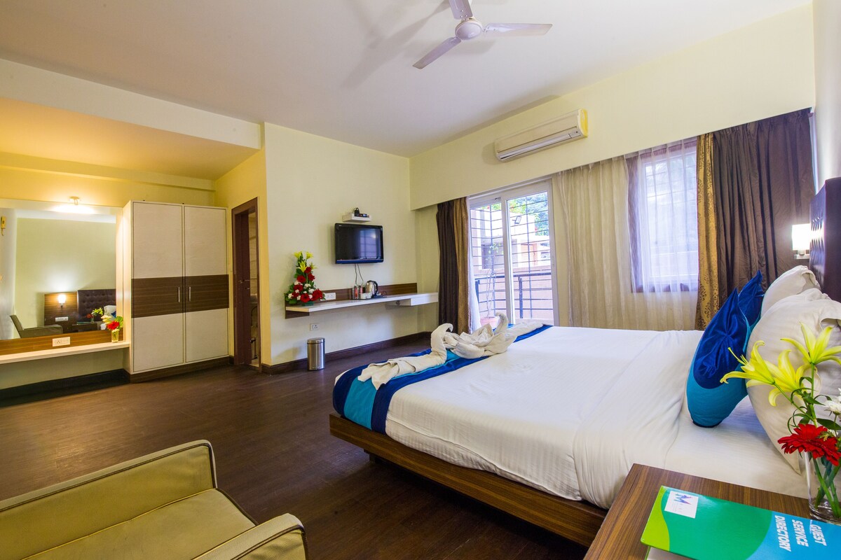 A hotel room with a bed, a desk, a chair, a TV, and a window with curtains.