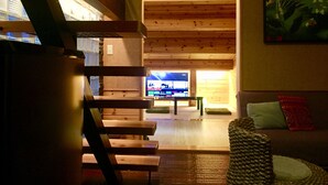 A cozy living room with wooden beams, a television, and a couch with cushions.