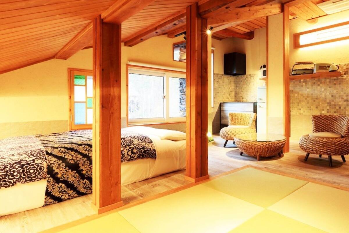 Una habitación tradicional japonesa con suelo de tatami, techo de madera bajo y una cama con colcha estampada.