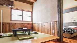 A traditional Japanese room with tatami flooring, a low wooden table, and a bed with a floral bedspread.