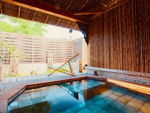 Een traditionele Japanse onsen met een houten terras, een stenen muur en een bamboebegraafsel.