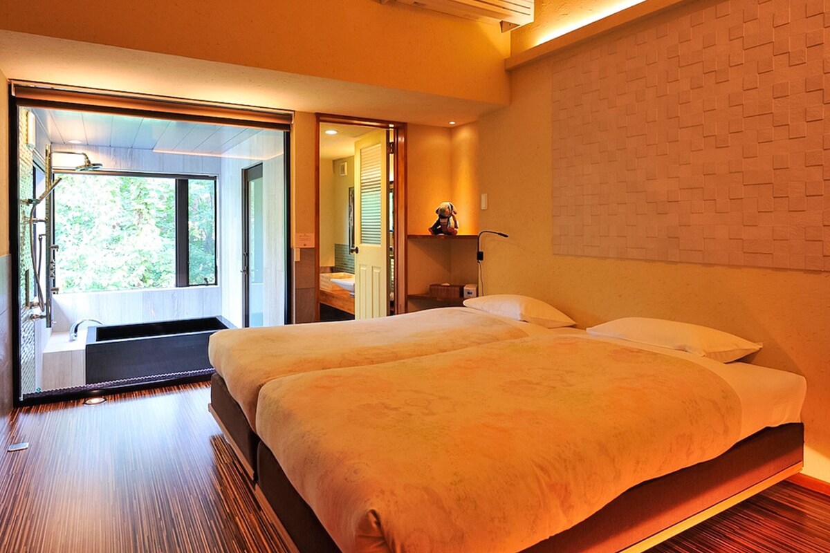 Habitación de hotel con una cama grande, baño con espejo y puerta corrediza que da a un espacio exterior.