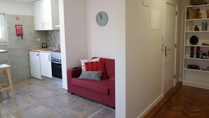 A compact living space with a kitchenette, a red sofa, and a clock on the wall. - Lisbon Beach Apartments 2. Beach 500 Mts, terrace, barbecue, pets welcome. (Costa da Caparica)