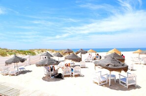 A beach with thatched umbrellas and white lounge chairs.