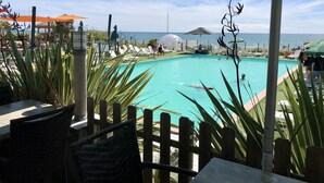 Ein Poolbereich mit Liegestühlen und Sonnenschirmen, umgeben von Holzzaun und tropischer Bepflanzung.