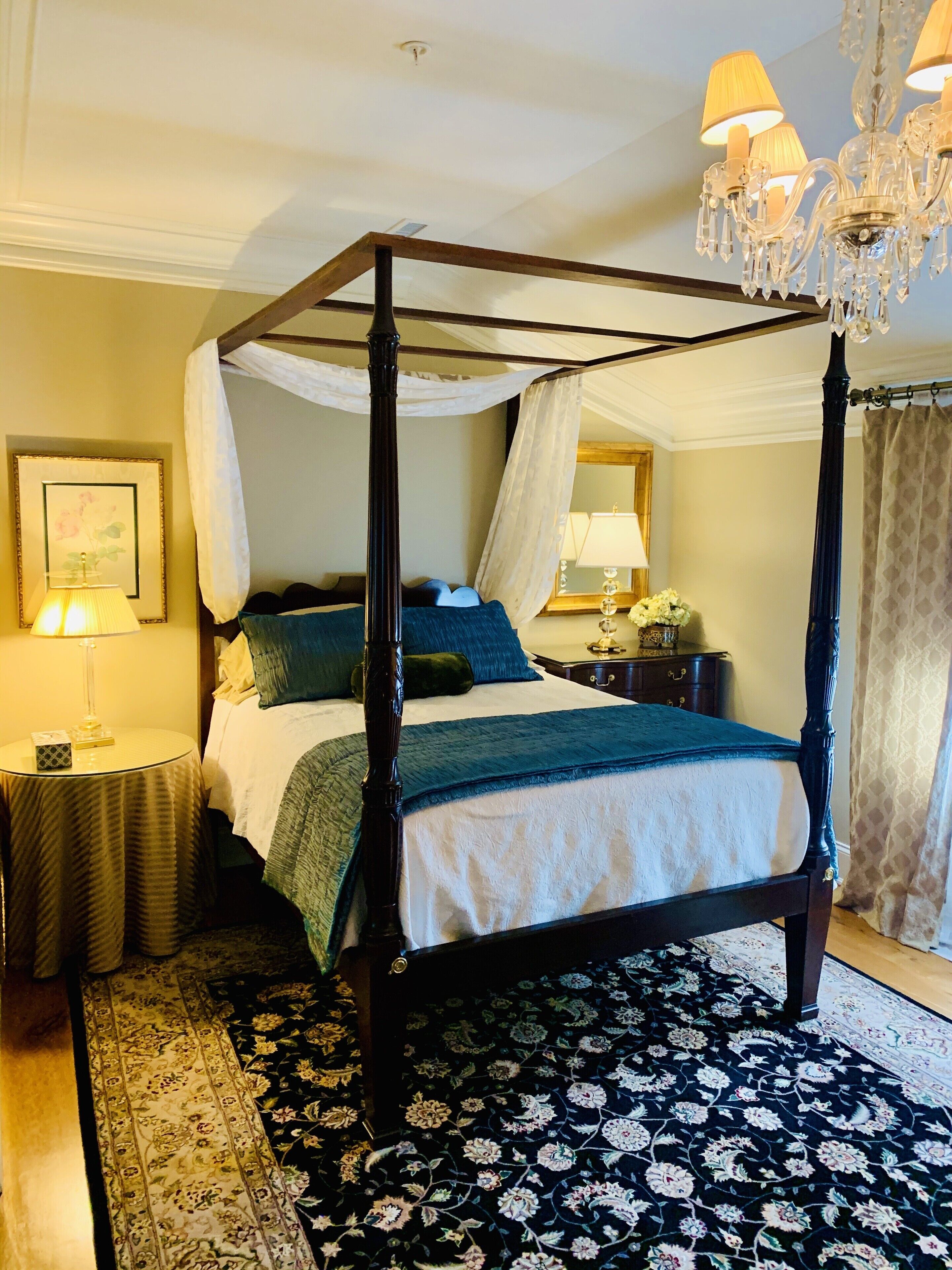 A four-poster bed with a canopy, a chandelier, and a floral-patterned rug.