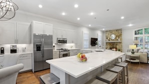 A modern kitchen with white cabinetry, stainless steel appliances, and a central island with stools. - Modern Tudor with Pool & Backyard Oasis on the M Streets in the Heart of Dallas (Dallas)