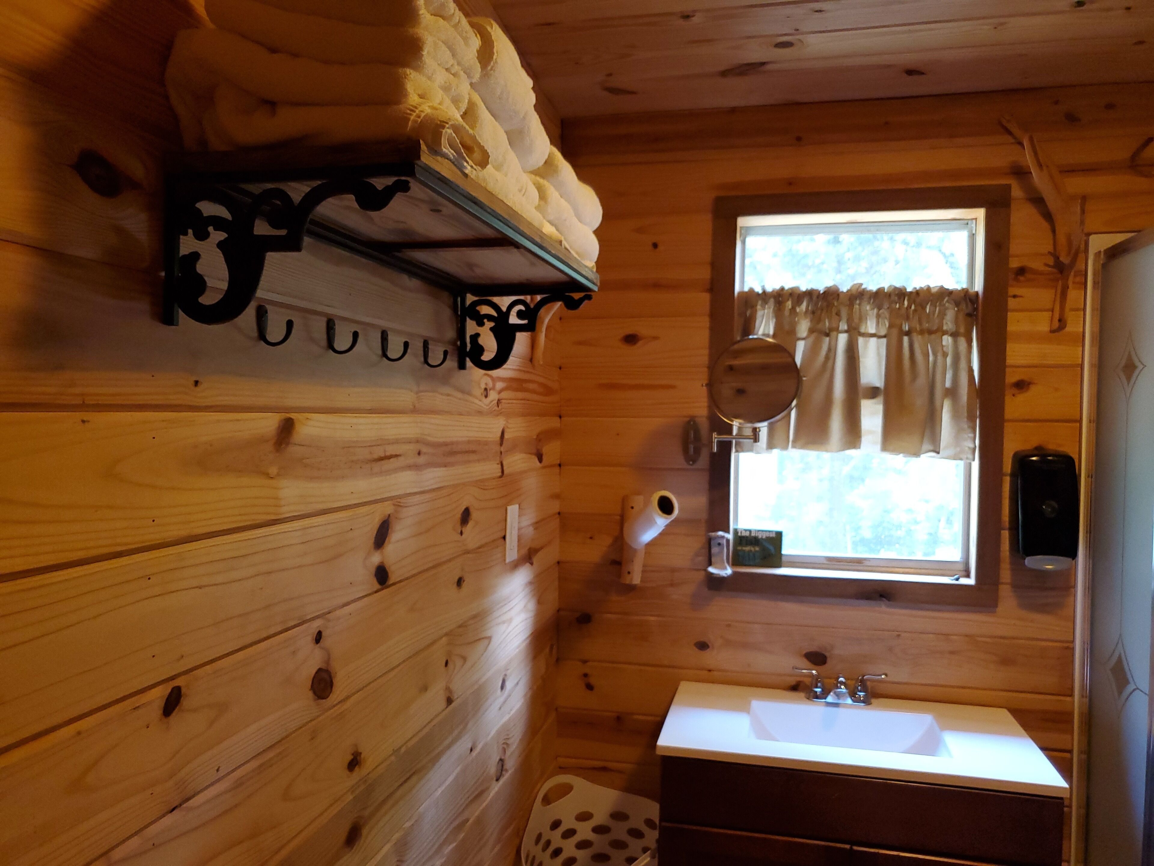 Une salle de bain rustique, avec des murs en bois, comprenant un lavabo, une fenêtre et un porte-serviettes.