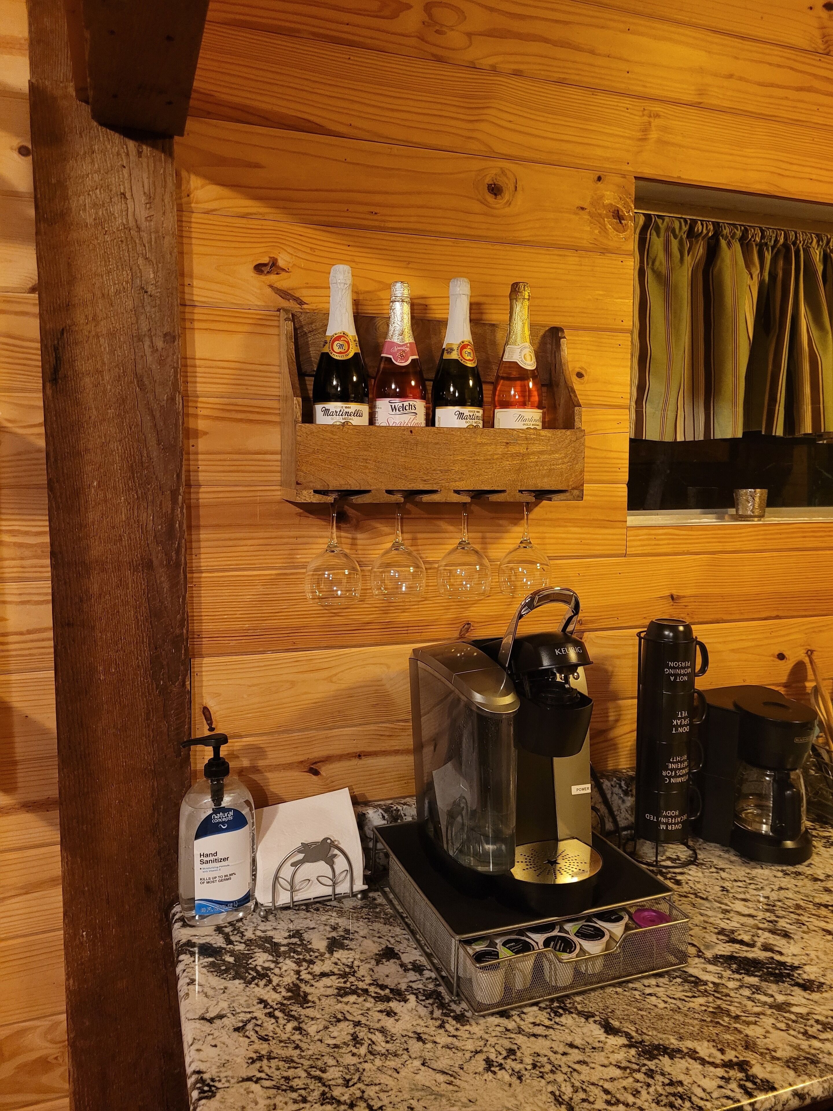 Pared de madera con un botellero que contiene cuatro botellas y copas debajo.