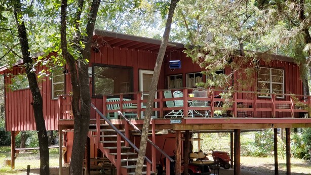 A rustic cabin with a wooden deck, outdoor seating, and a staircase leading to a second level. - Treehouse Cabin/ Beach and Lake Access (Pottsboro)
