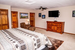 Une chambre à coucher comprenant un lit, une commode en bois, une chaise, un téléviseur et un ventilateur de plafond.