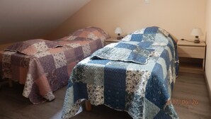 Une petite chambre accueillante, avec deux lits, chacun recouvert d’une couverture à motifs différents. On y trouve des tables de chevet avec des lampes, et une lucarne au-dessus des lits.