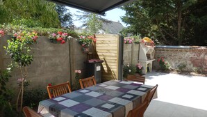 Une terrasse extérieure avec une table dressée pour quatre personnes, entourée de chaises en bois.