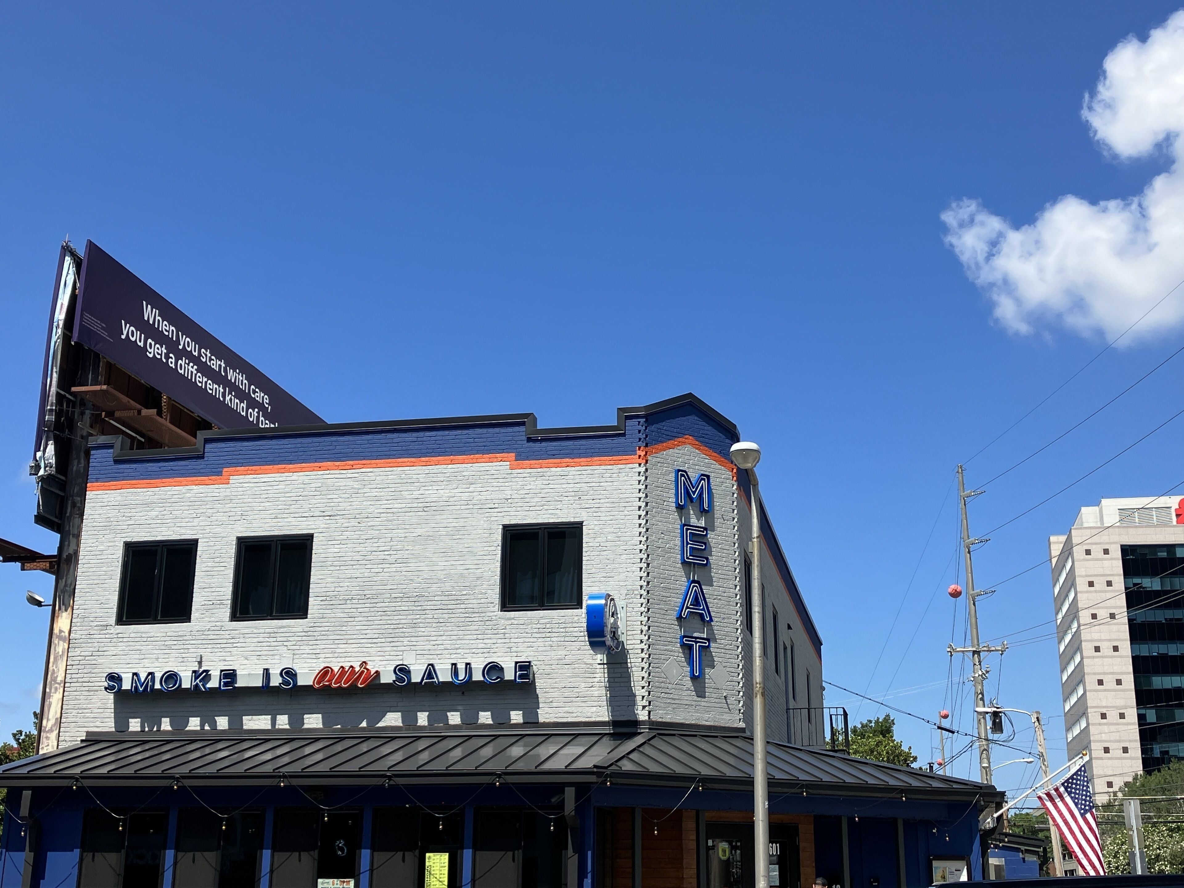 A building with a sign that reads "MEAT" and another sign that says "SMOKE IS OUR SAUCE".
