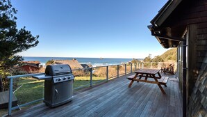 Une terrasse en bois avec un barbecue et une table de pique-nique, offrant une vue sur la côte.