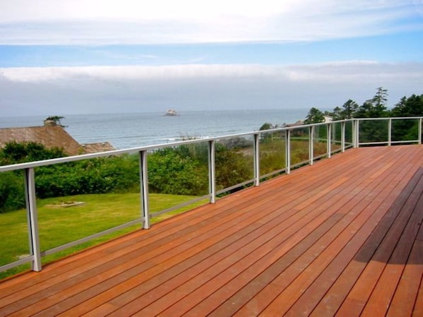 A wooden deck with a metal railing overlooking a coastal landscape with greenery and a distant island.