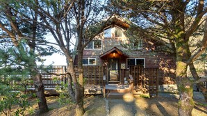 Une cabane avec une façade en bois, un porche à l’avant et une cour clôturée.