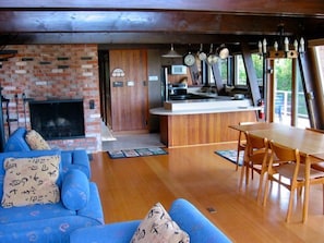 A cozy living room with a fireplace, a dining area with a wooden table and chairs, and a kitchen with hanging pots and pans.